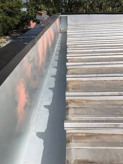 Corrugated metal roof draining into a light metal box gutter beside a parapet