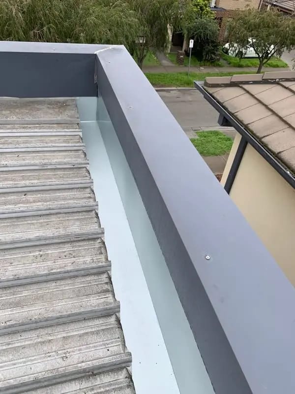 Looking down a light metal box gutter between corrugated roofing and a dark-capped parapet