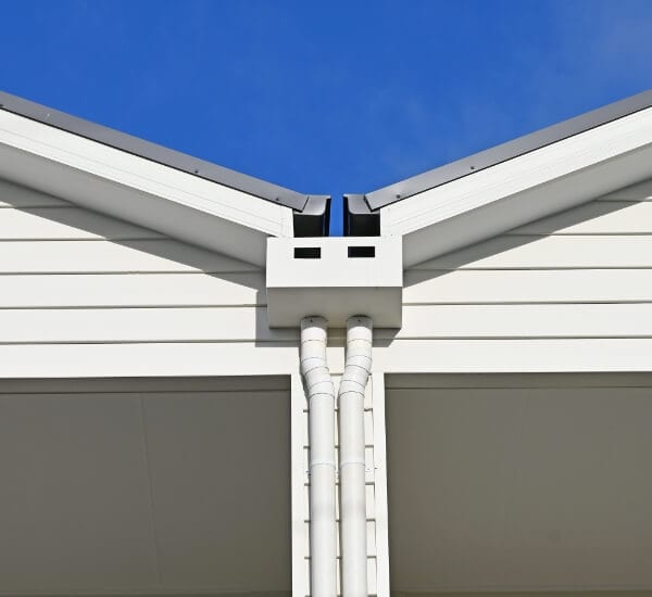 White rainhead with overflow slots and two downpipes at a dark metal gable junction