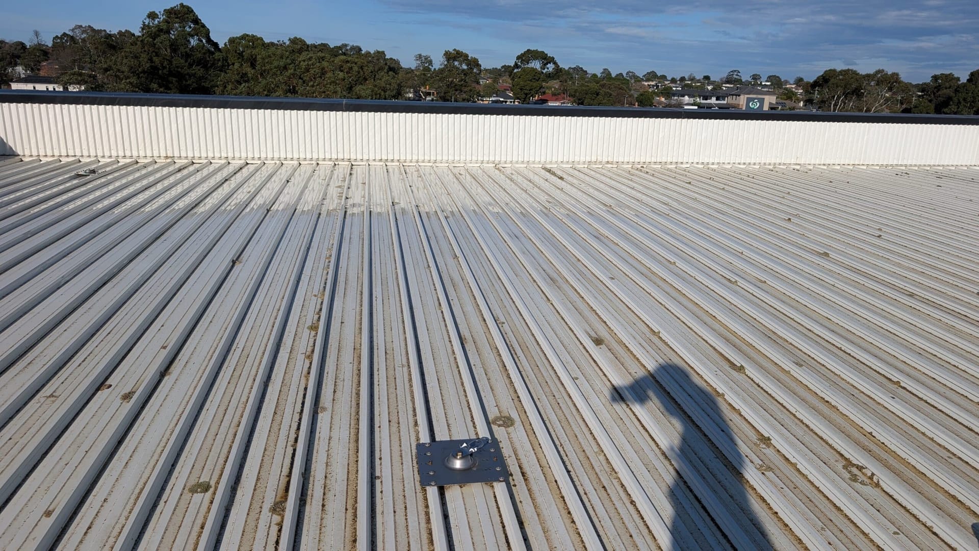 White corrugated metal roof with dirty channels and a safety anchor, shops in the background