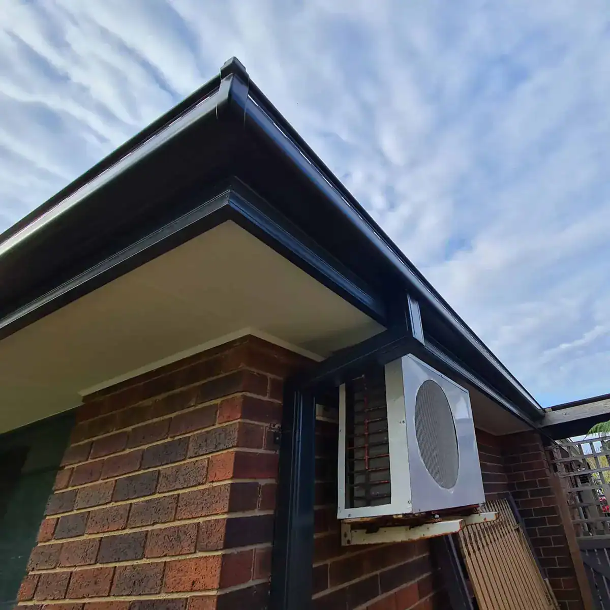 Brick corner with a new black gutter, downpipe and white soffit