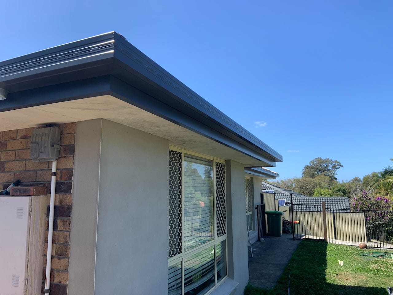Charcoal gutter and white soffit against a rendered wall