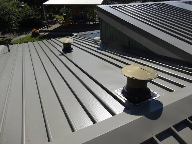 Light ribbed metal roof with vents on a low-pitch residential roof