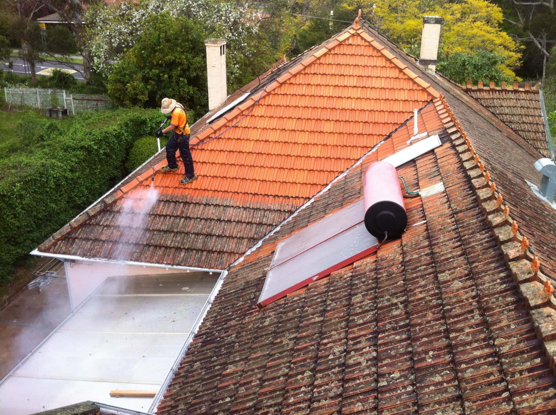 Roofer in high-vis and a harness pressure-washing a residential tiled roof