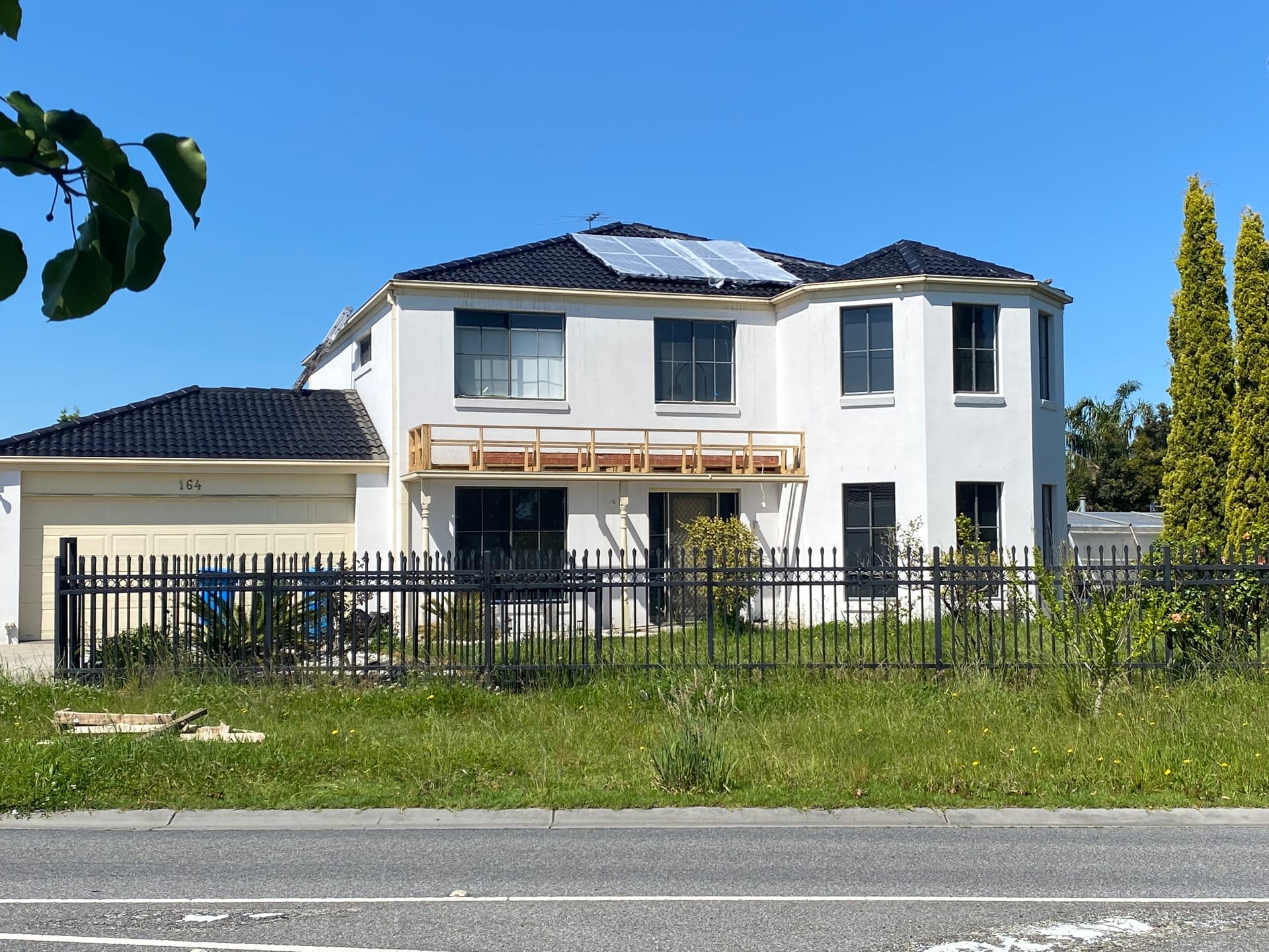 House number 164 from the street with tarp on the roof and a timber balcony frame