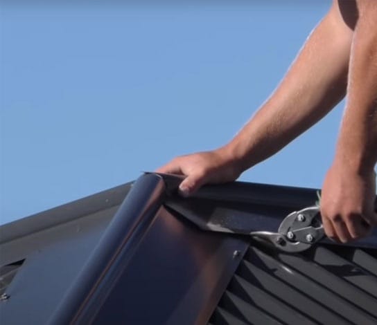 Hands cutting dark metal flashing with snips on a corrugated metal roof