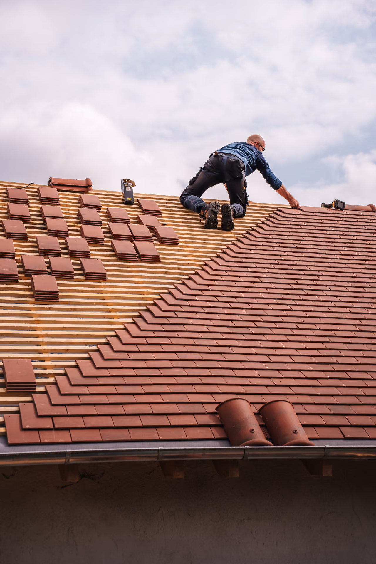 Roofer laying terracotta tiles onto battens, photographed from behind