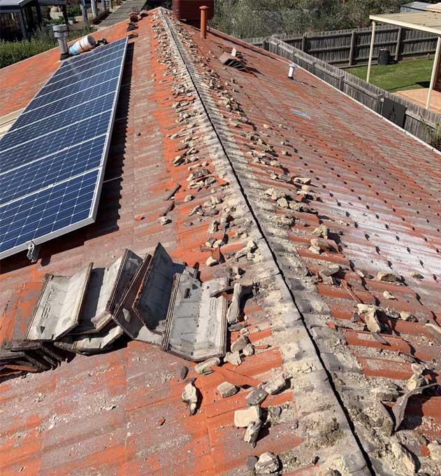 Tiled roof mid-restoration with ridge caps off, mortar debris and a solar array