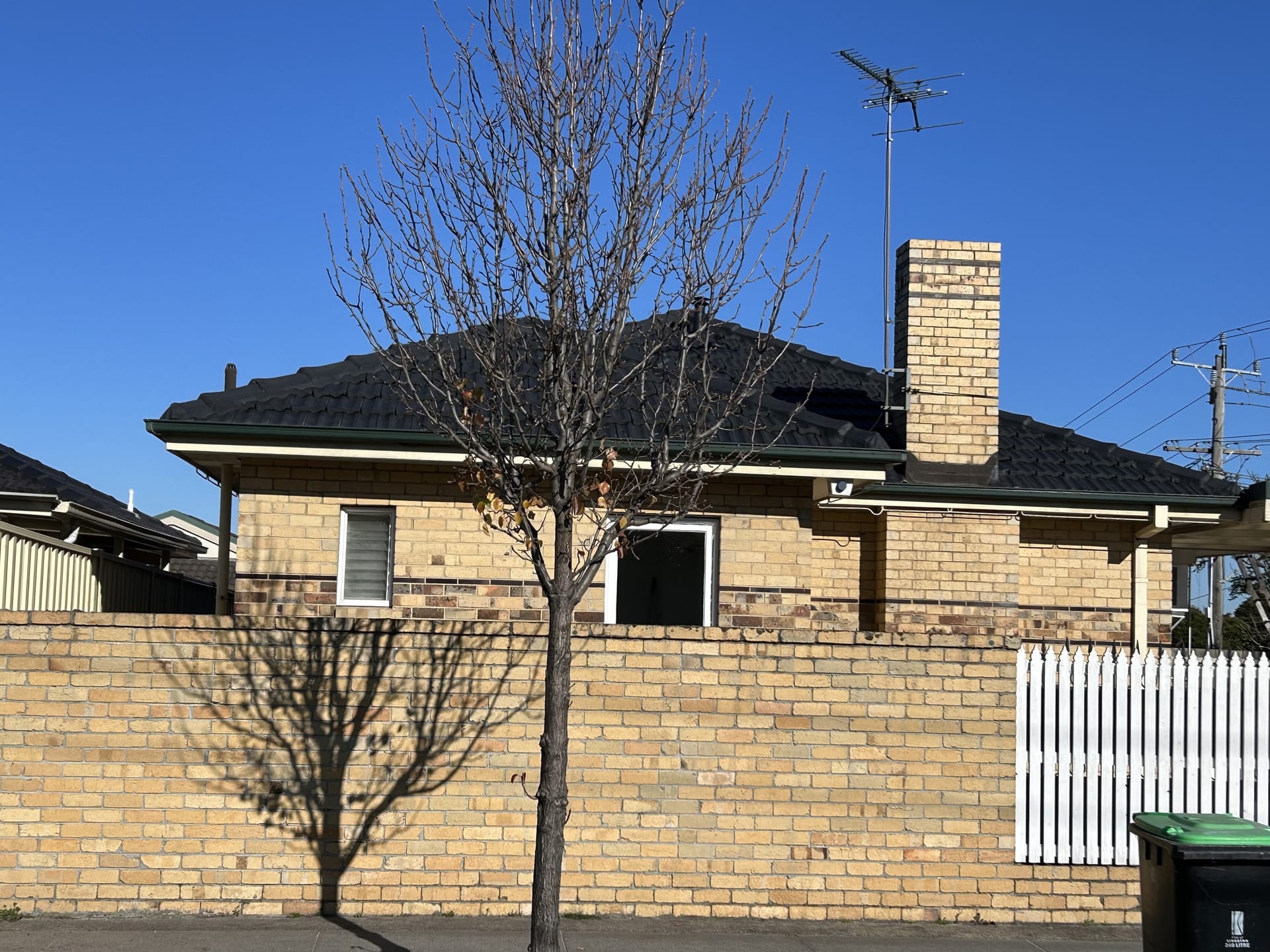 Brick Melbourne house with a dark tiled roof, green gutters and chimney, photographed from the street