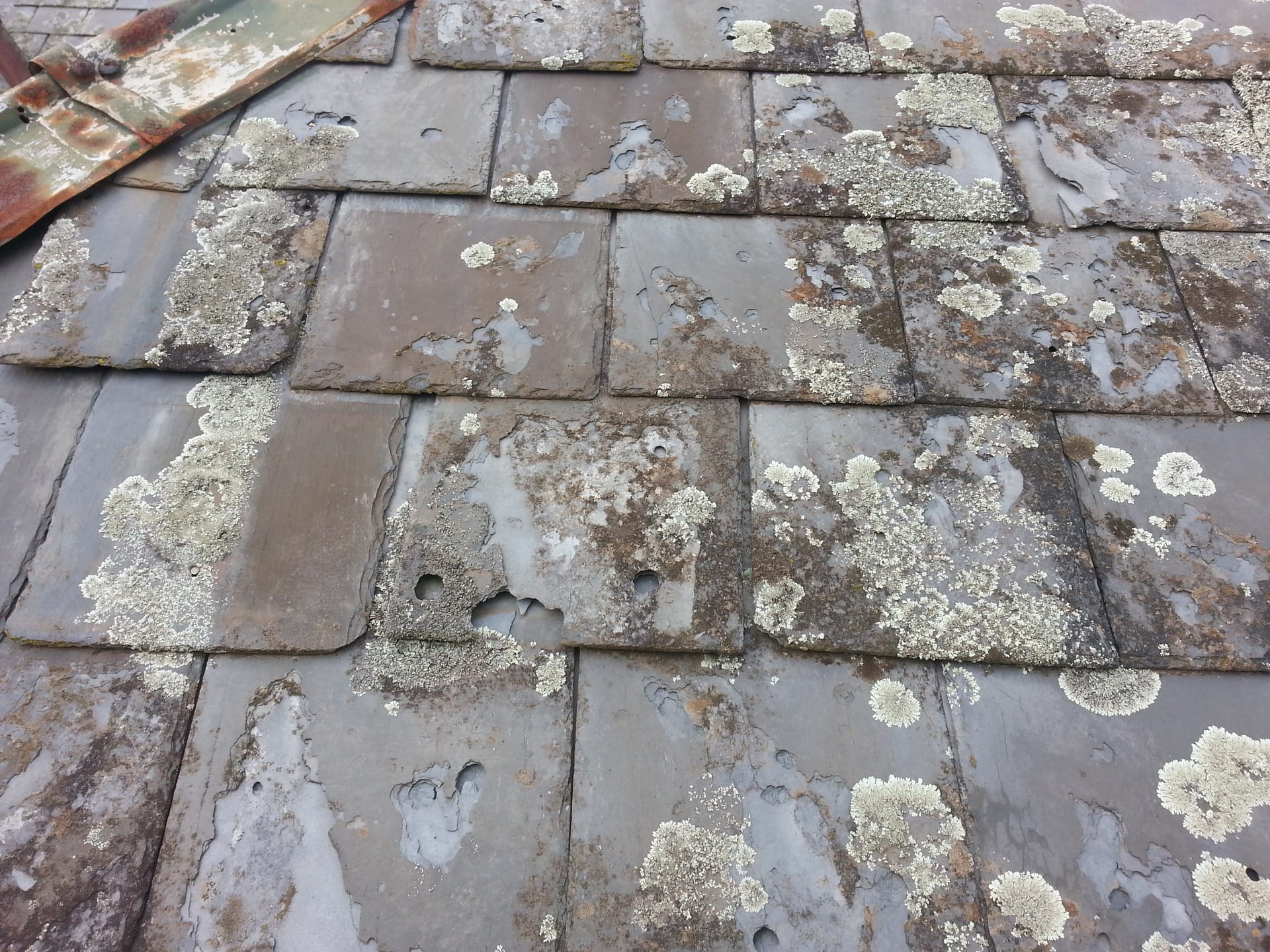 Close-up of aged slate with flaking surfaces, holes through the stone and rusted metal at the edge