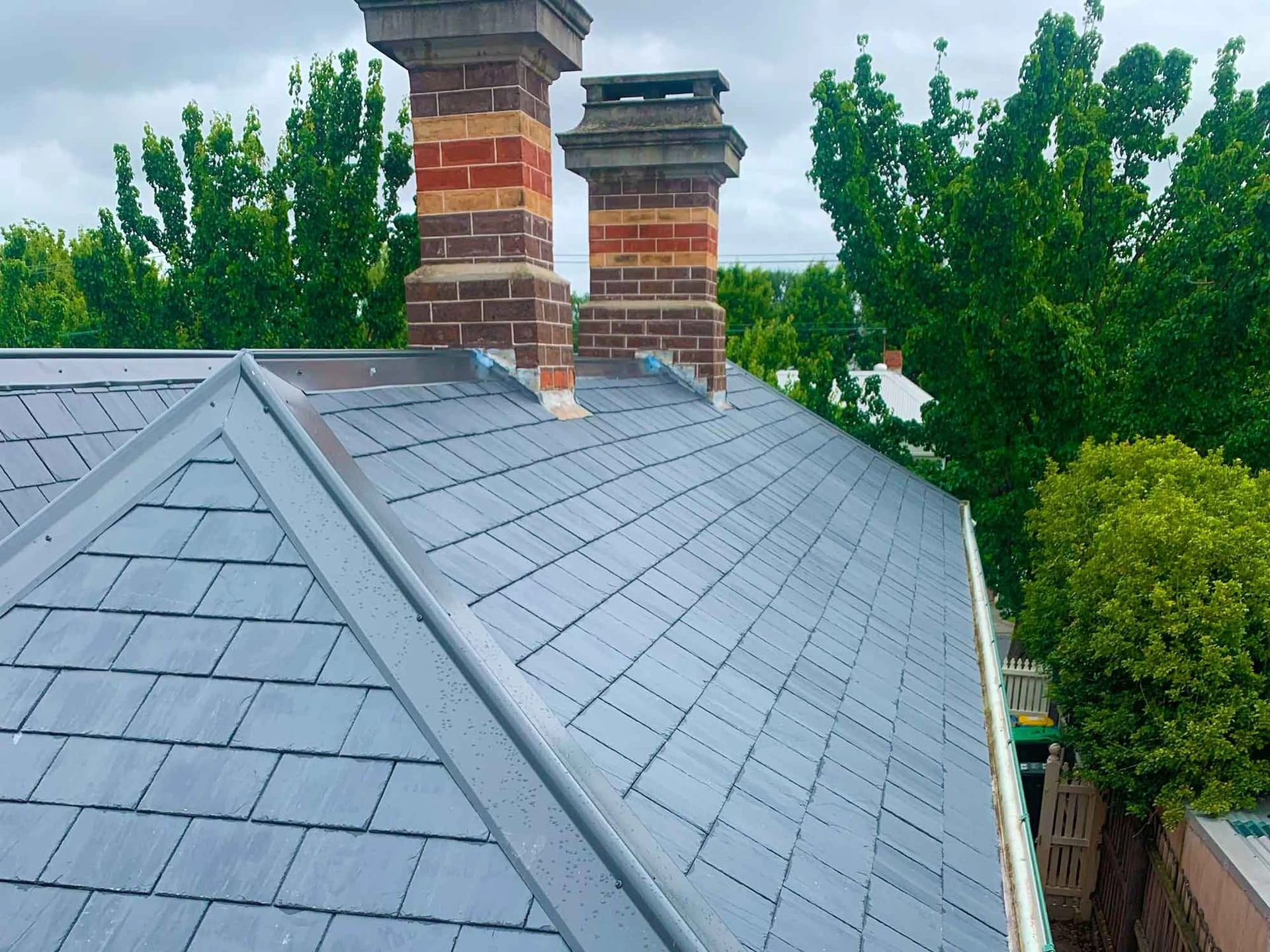 Dark slate roof with two banded brick chimneys, lead flashings and metal hip capping