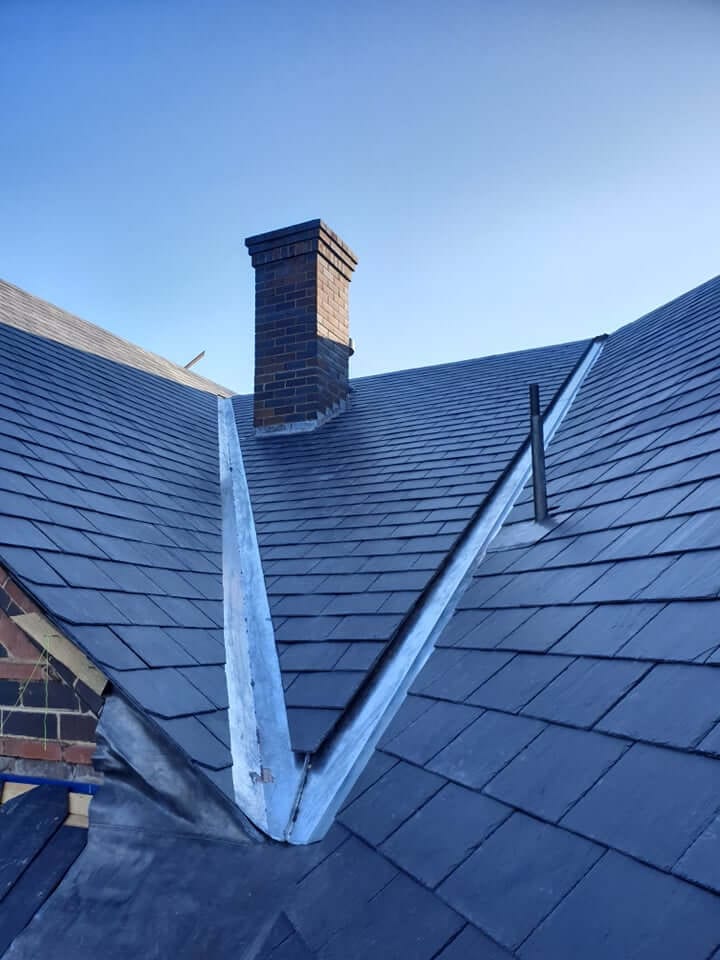 Dark slate roof with lead valleys meeting at a brick chimney